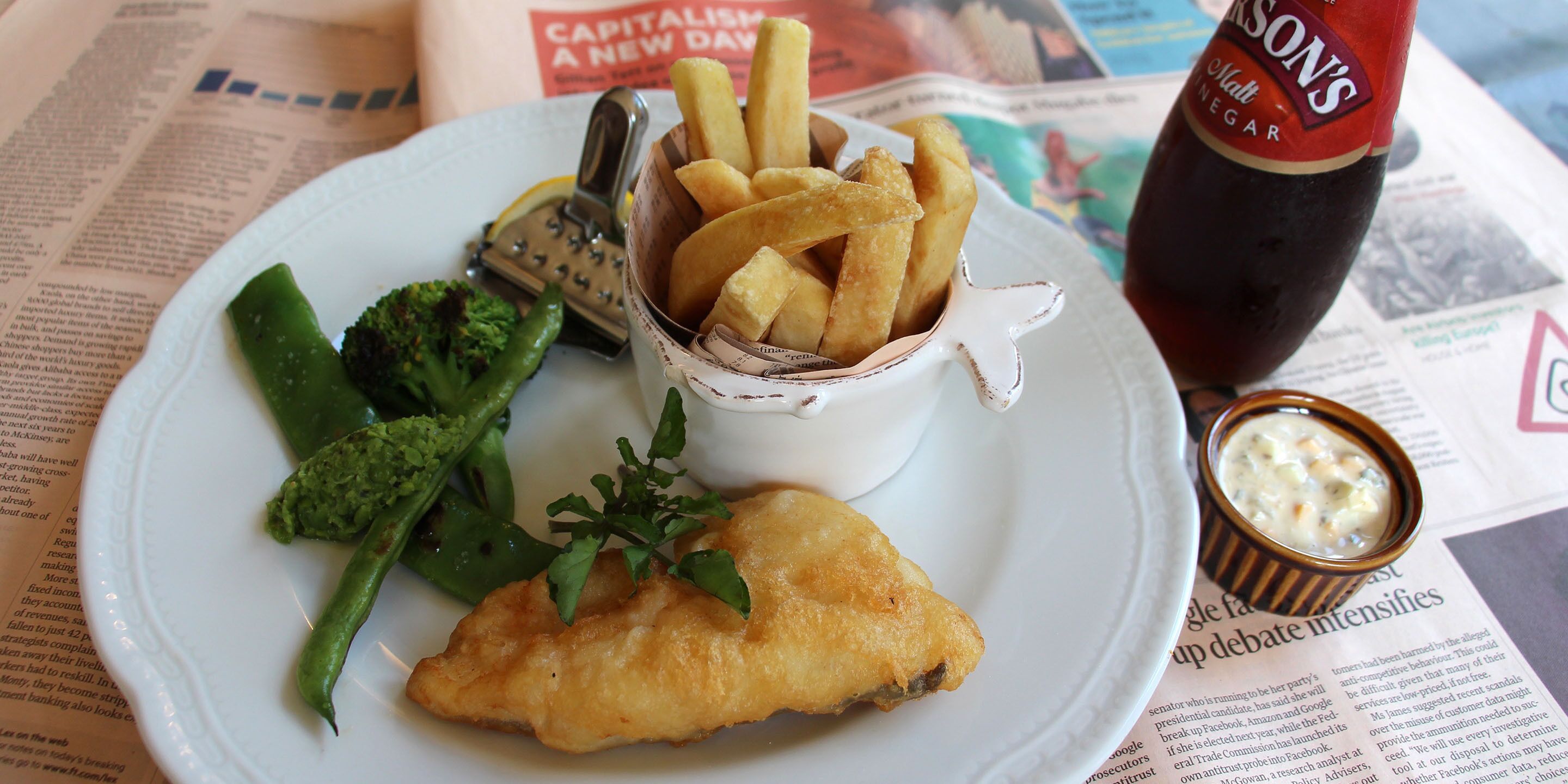 A plate with fish and chips, a small bowl of tartar sauce, and a bottle of vinegar.