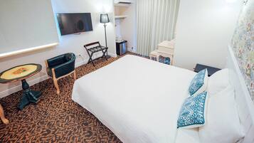 A hotel room with a large bed, a small table, a chair, a TV, and a window with curtains.