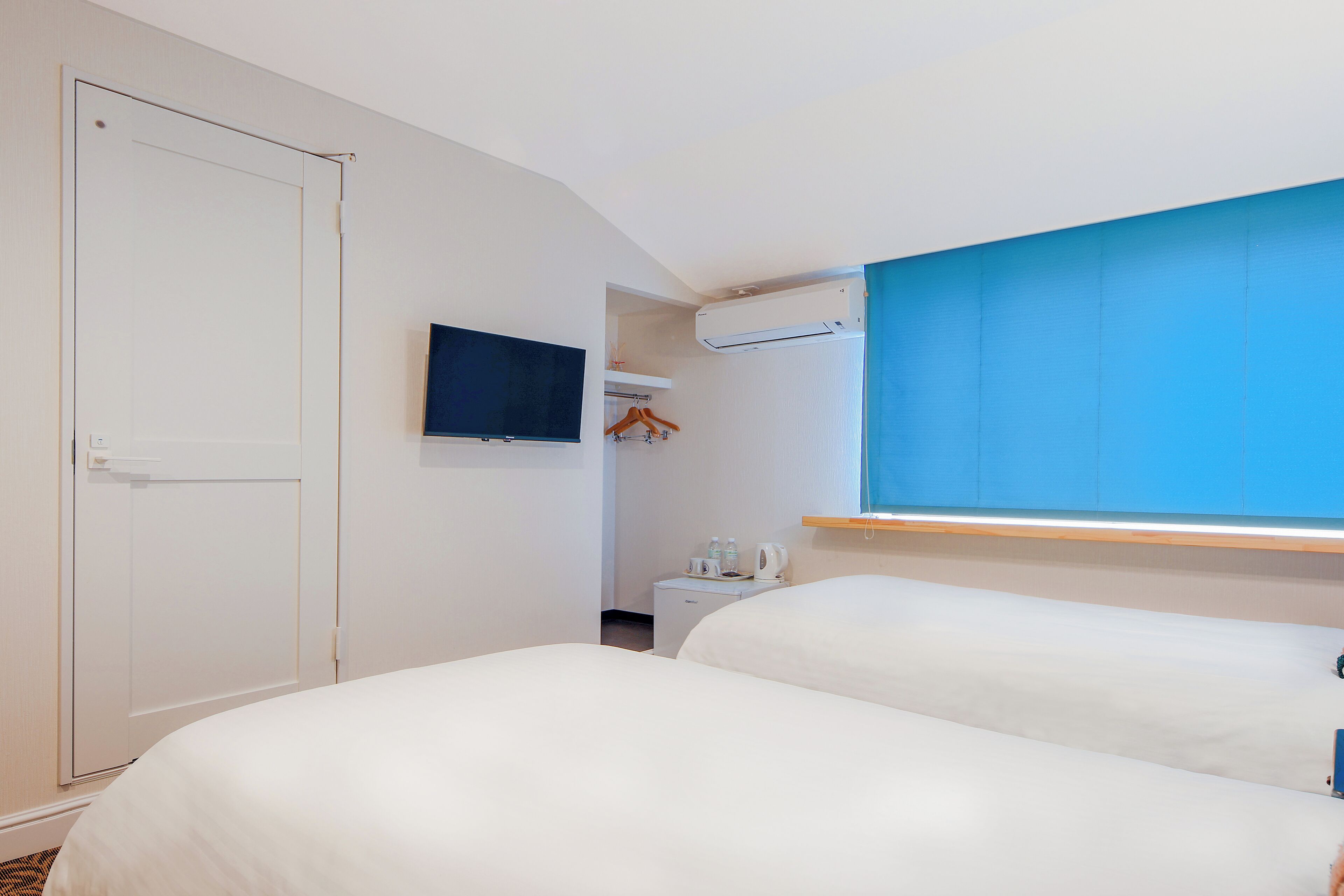 A hotel room with two beds, a television, a small table with a kettle, and a wardrobe.