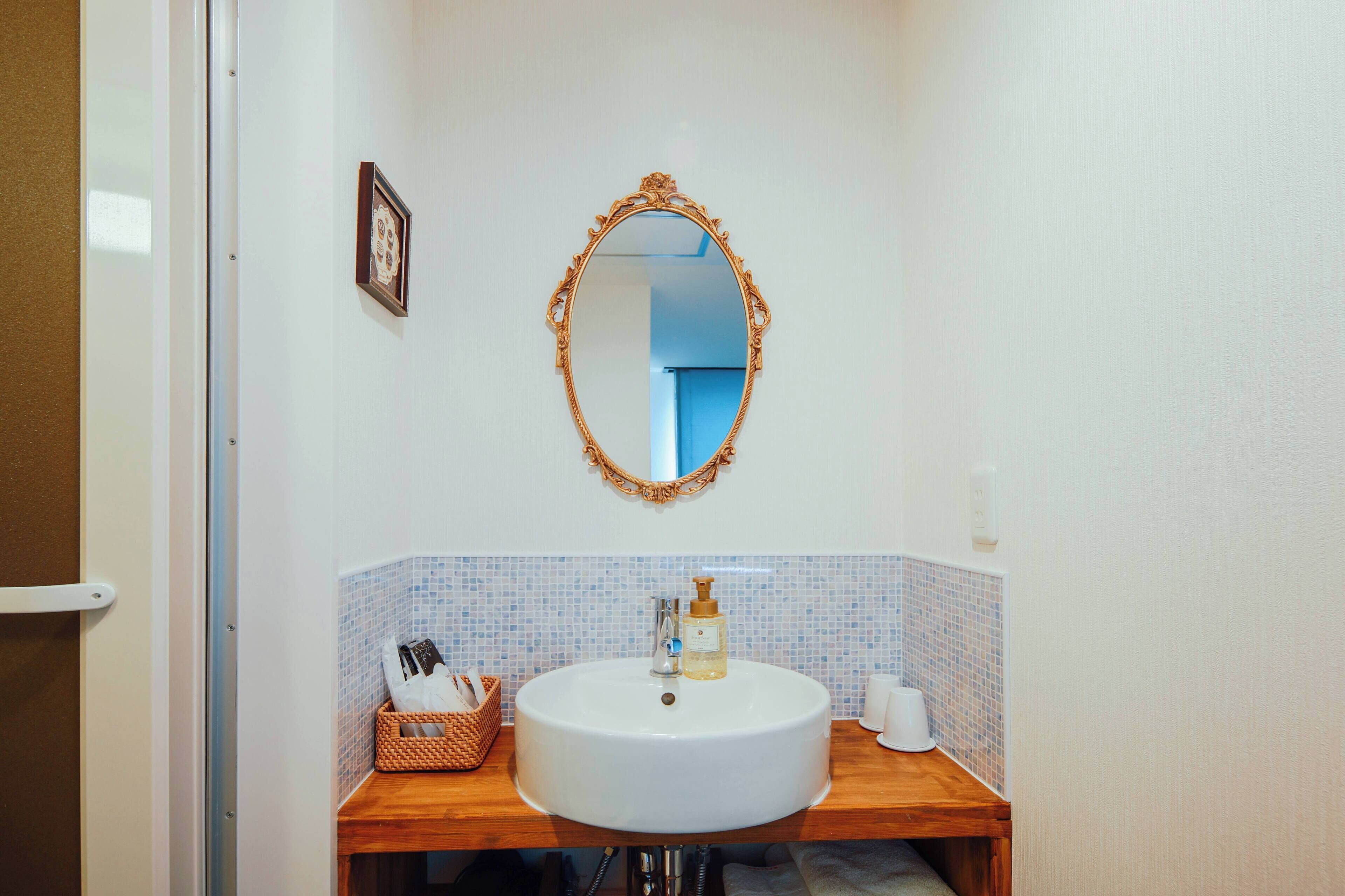A bathroom with a round white sink, a wooden vanity, a mirror with an ornate frame, and a small basket on the counter.