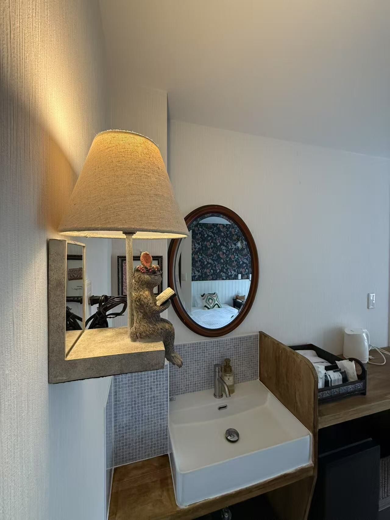 A bathroom with a wall-mounted mirror, a round mirror, a sink, and a lamp.