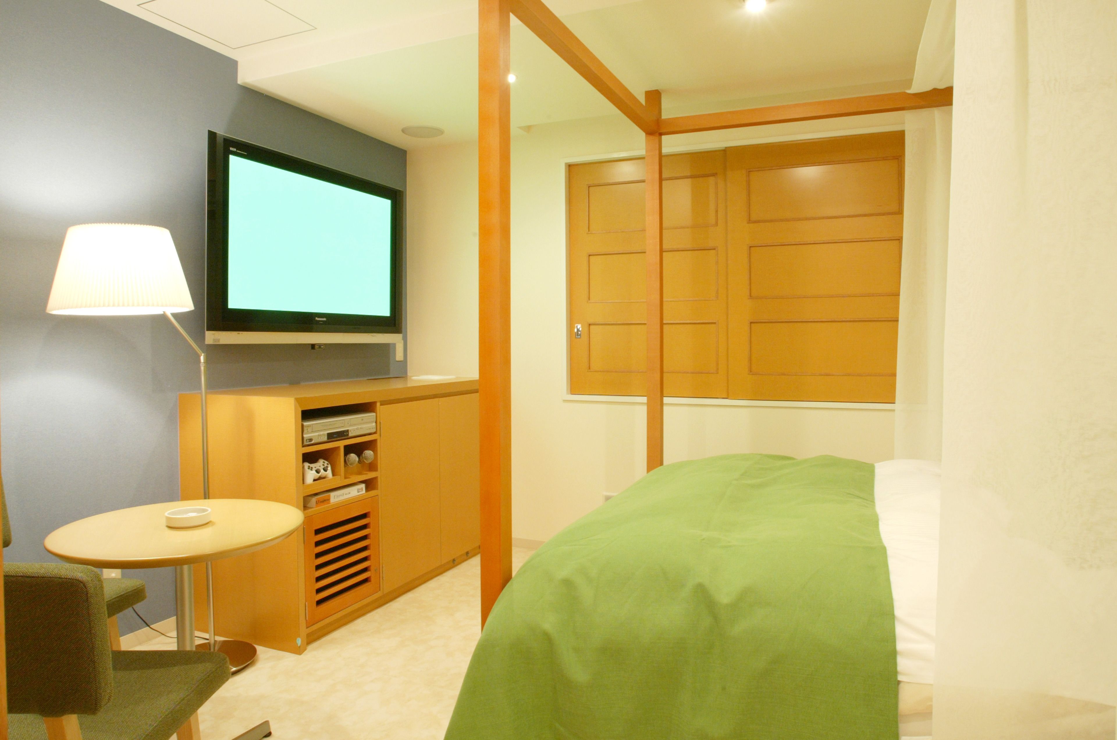 A bedroom with a bed, a television on the wall, a small table, and a cabinet.