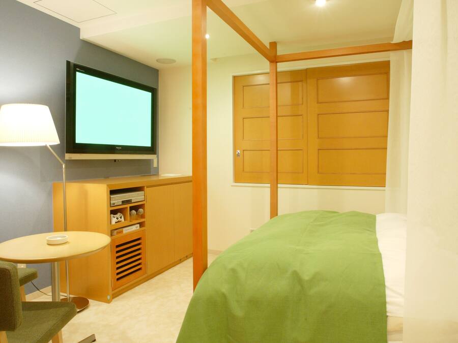 A bedroom with a bed, a television on the wall, a small table, and a cabinet.