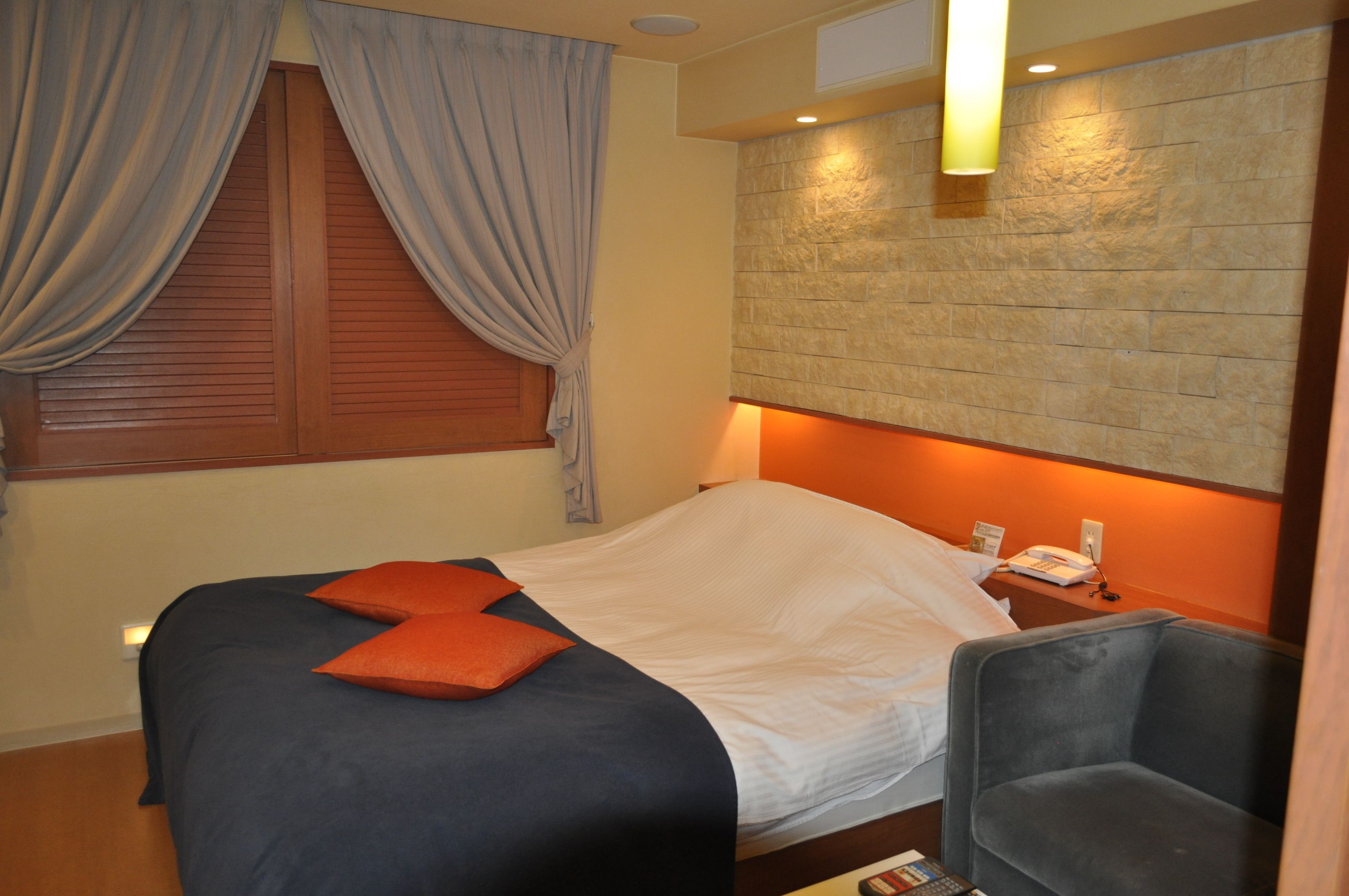 Una habitación de hotel con cama, sillón, mesita de noche y teléfono en la pared.