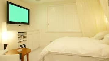 A bedroom with a bed, a television mounted on the wall, a bedside table, and a window with curtains.