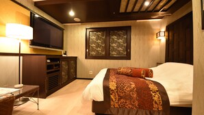 A hotel room with a bed, a TV mounted on the wall, a desk with a lamp, and a window with decorative shutters. - HOTEL WOO - Adults Only (Yamatotakada)