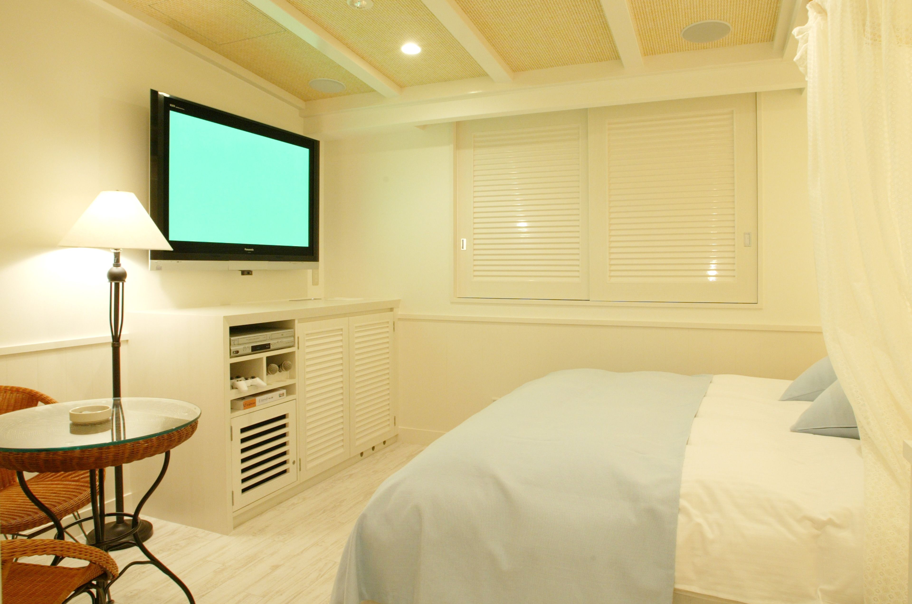 Una habitación de hotel con cama, televisión en la pared, una mesa con sillas y una ventana con persianas.