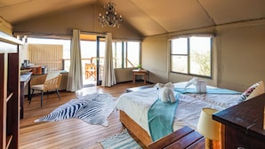 A spacious room with a large bed, a desk, and a chair. There is a view of the outdoors through the windows. - Windhoek Game Camp (Windhoek)