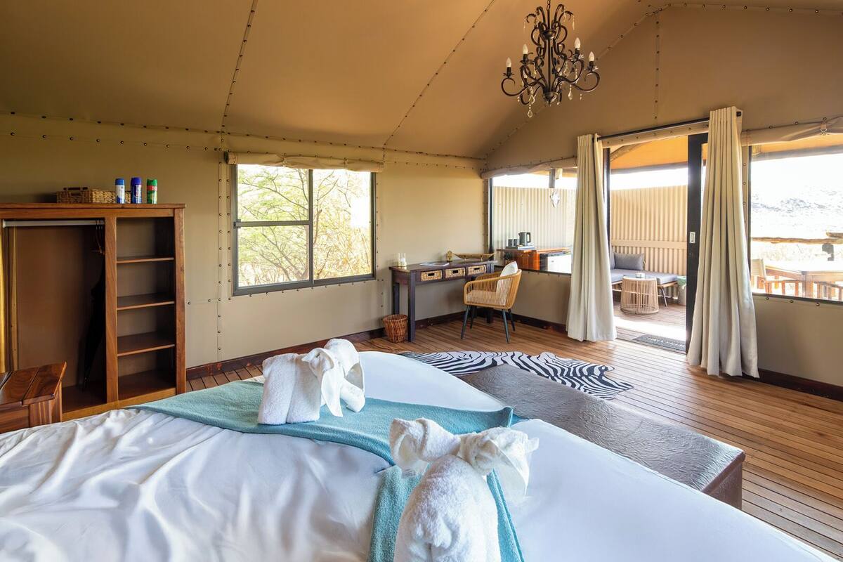 A bedroom with a bed, a desk, a chair, and a view of the outdoors.