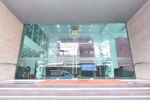 A modern building with a glass facade, a logo at the entrance, and a staircase leading up to the entrance. - Mayflower Grande Hotel Hat Yai (Hat Yai)