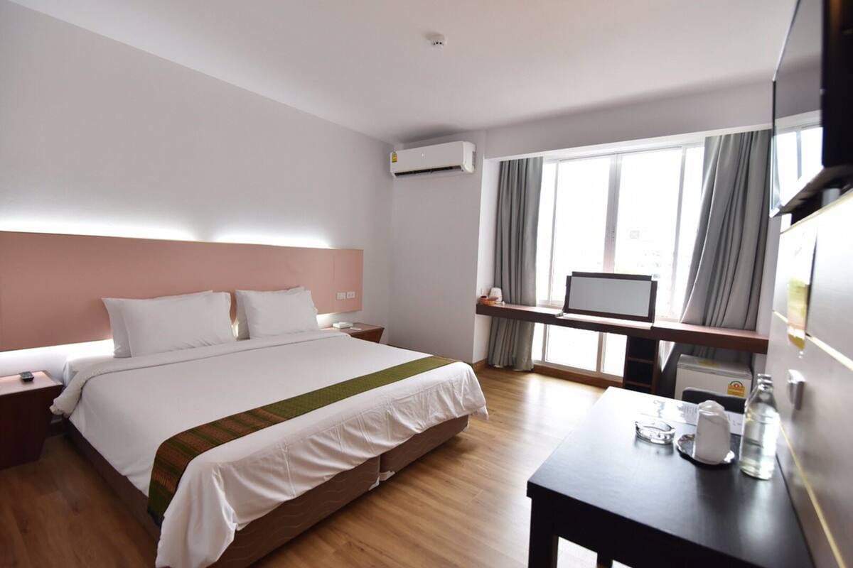 Une chambre d’hôtel avec un lit, une table de chevet, une télévision et une fenêtre avec des rideaux.