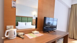 A hotel room with a wooden desk, a television, a kettle, and a bed with a green headboard. - Mayflower Grande Hotel Hat Yai (Hat Yai)