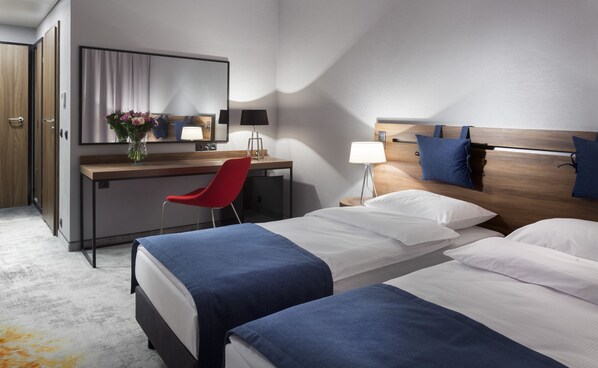 Una habitación de hotel con dos camas, un escritorio, una silla y un espejo grande.
