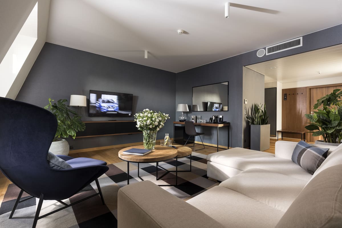 A modern living room with a sofa, armchair, and coffee table, a flat-screen TV, and a large mirror.
