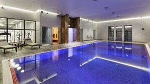 A large indoor swimming pool with a blue floor, surrounded by lounge chairs and a glass partition. - Hotel Sadova (Gdansk)