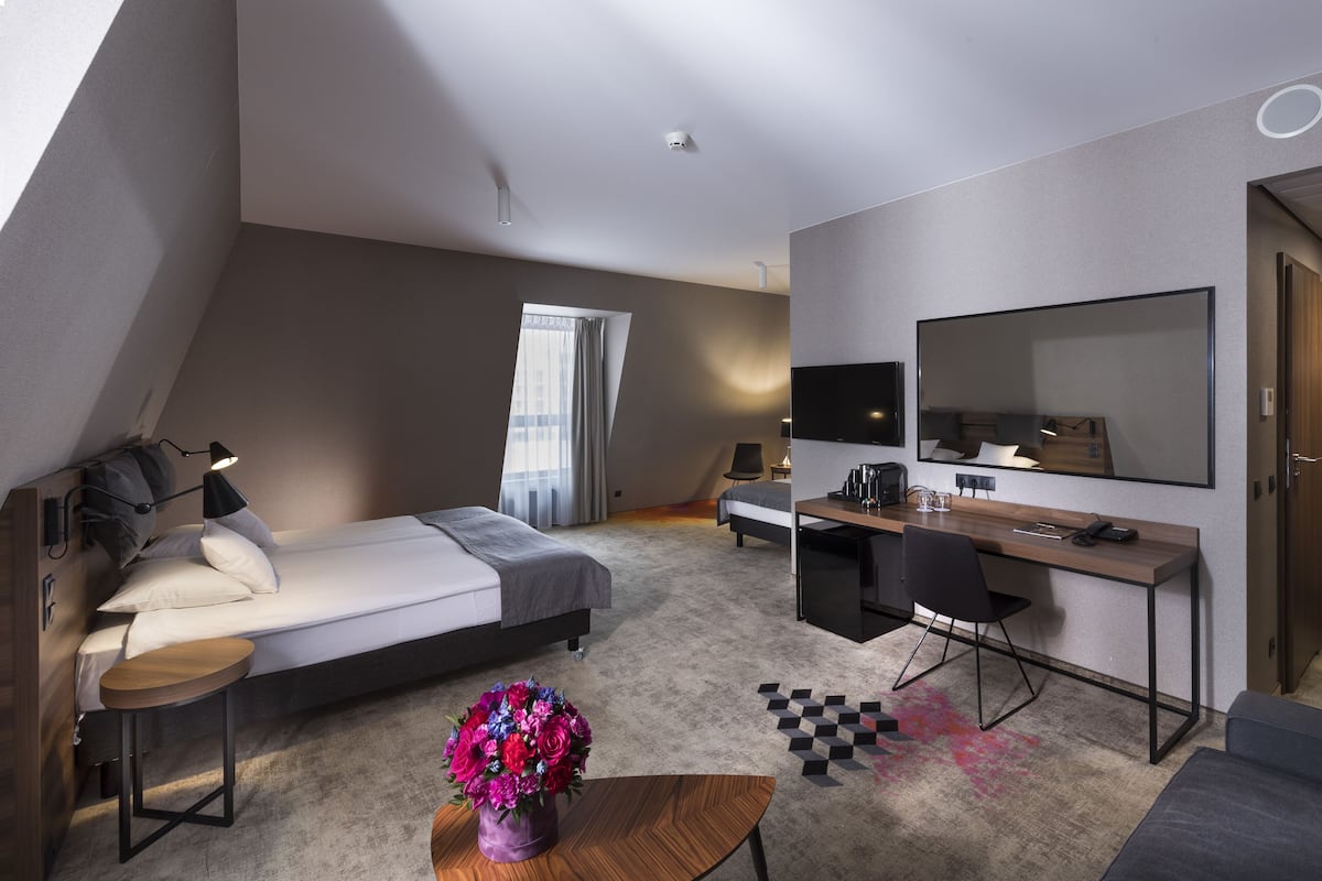A modern hotel room with a bed, desk, chair, and a large mirror.