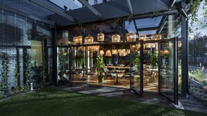 A modern outdoor dining area with glass walls, wicker furniture, and hanging lights. - Hotel Sadova (Gdansk)