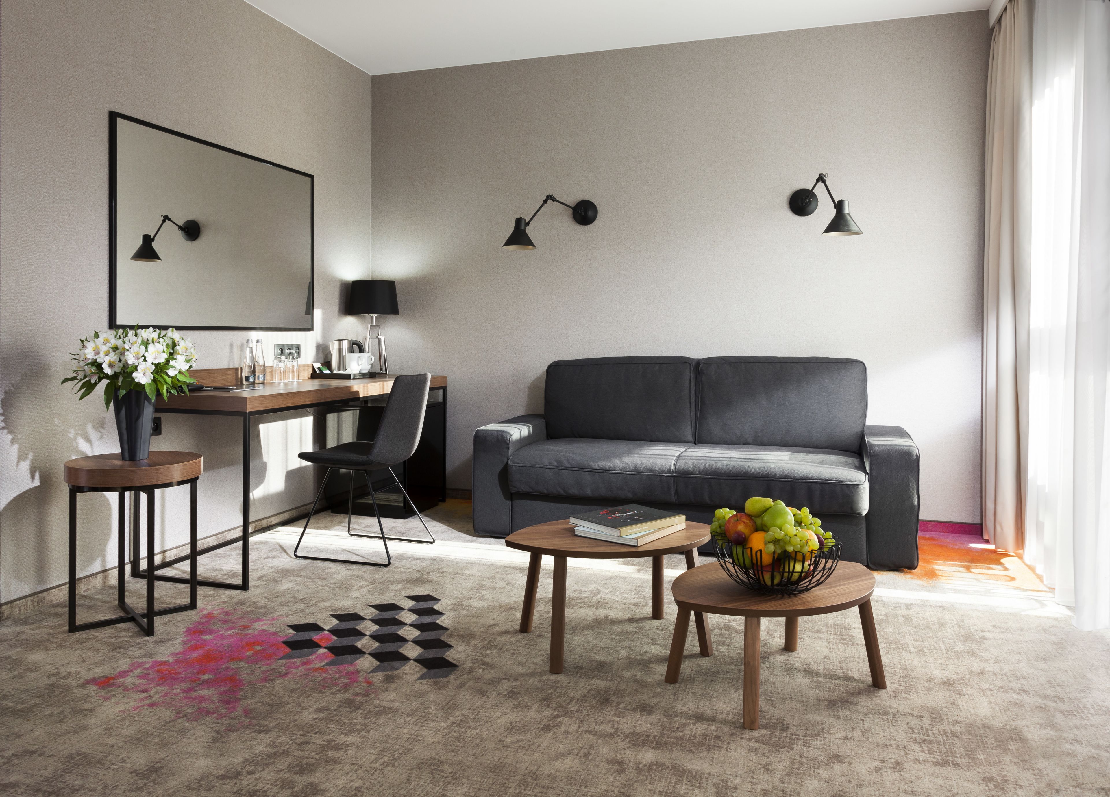 A modern living room with a sofa, a desk with a chair, a coffee machine, and a fruit basket on a coffee table.