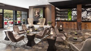 A modern lounge area with comfortable seating, a bar with a variety of bottles, and a large window offering a view of the outside. - Hotel Sadova (Gdansk)