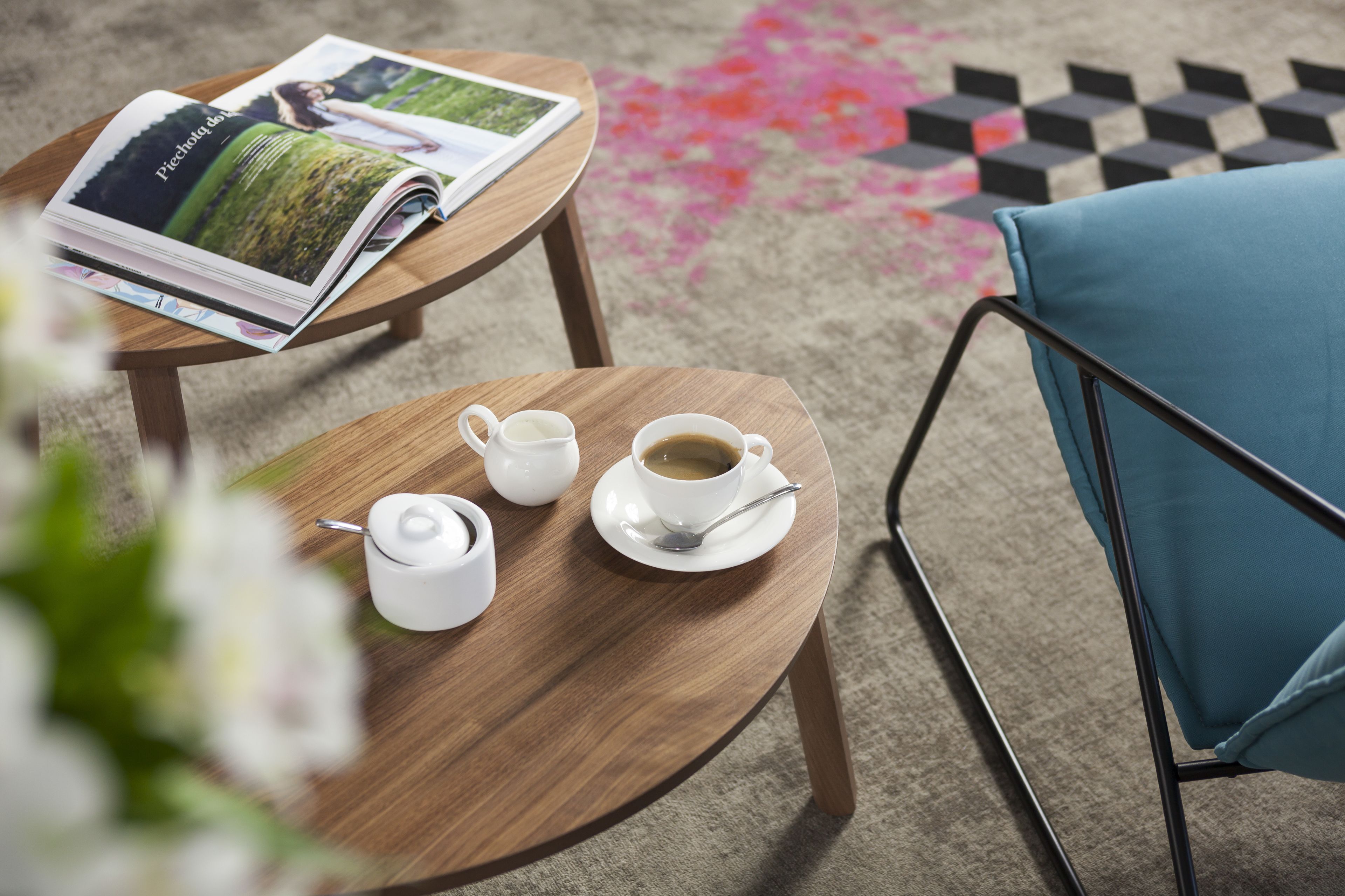 Ett träbord med ett tidningsställ, en tekanna, en kopp kaffe och en blå stol.