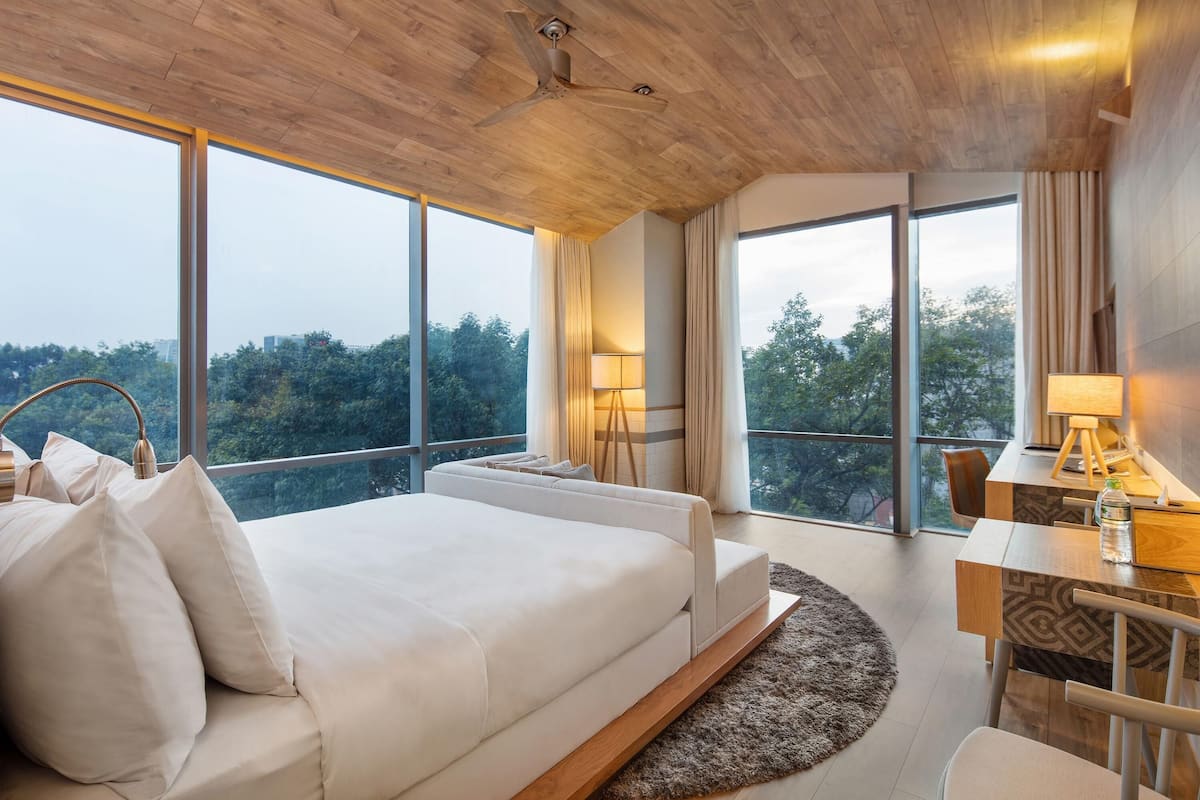 A modern bedroom with a large bed, a desk, and a view of the outdoors.