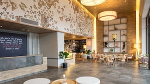 A modern lobby with a blackboard displaying a message, a reception desk, and a seating area with tables and chairs.