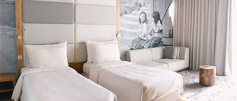 A modern bedroom with two beds, a sofa, and a large wall mural.