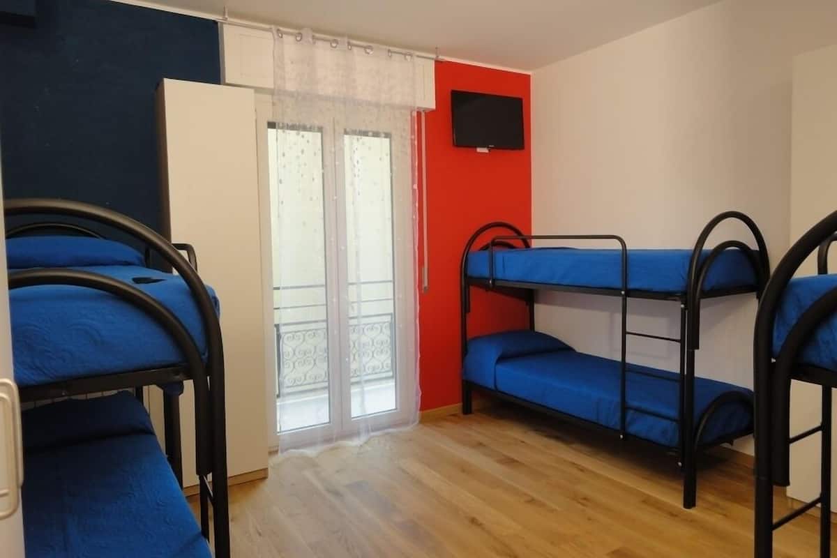 Une chambre de dortoir avec des lits superposés, un téléviseur fixé au mur et une porte-fenêtre coulissante donnant sur l’extérieur.