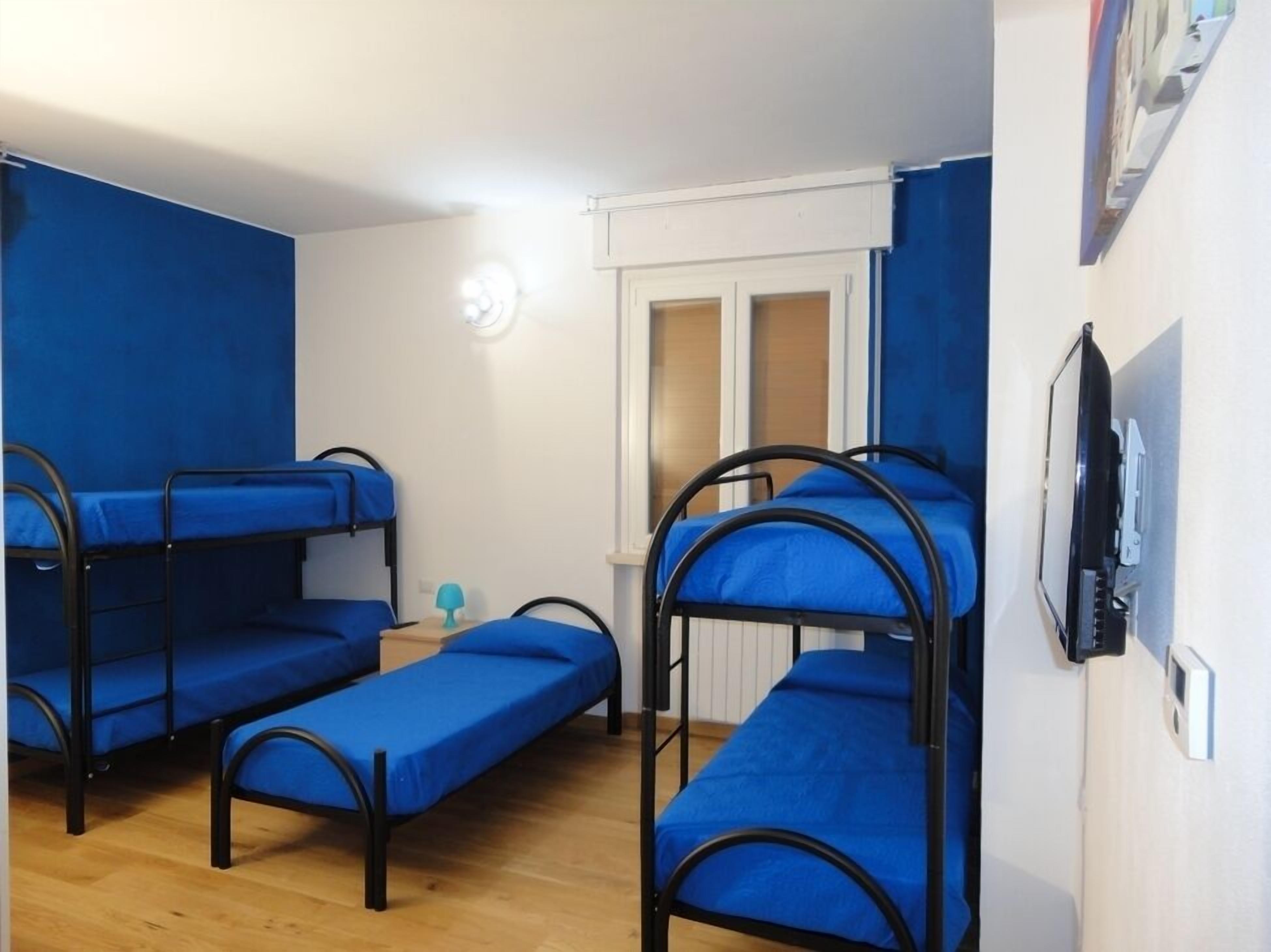 Habitación tipo dormitorio con literas y una cama individual, suelo de madera, ventana con persianas y televisión montada en la pared.