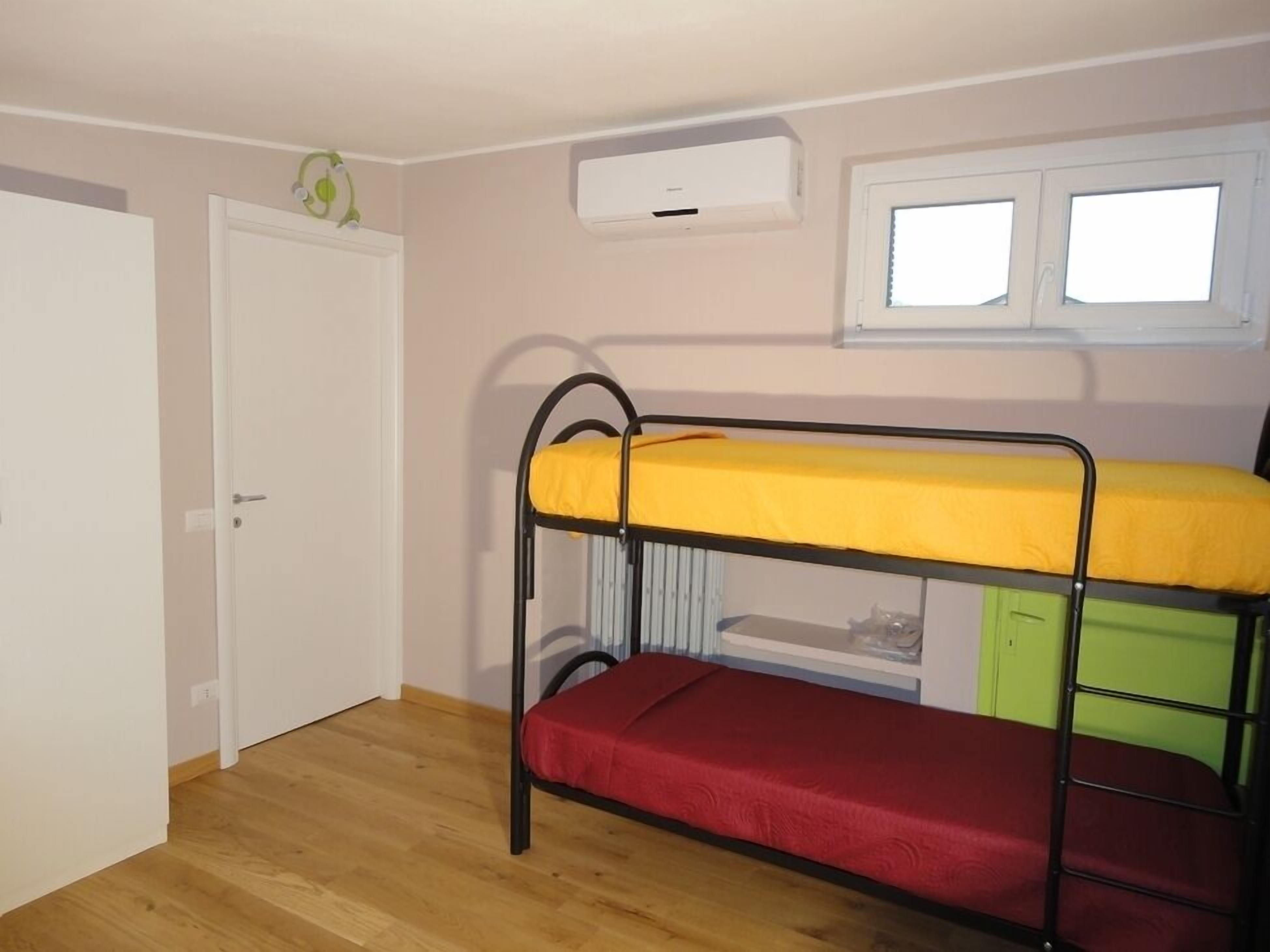 Dormitorio con literas, una puerta blanca, unidad de aire acondicionado y ventana con persianas.