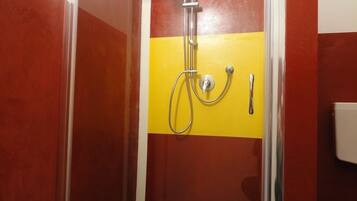 A shower enclosure with a yellow and red wall, a chrome showerhead, and a handheld showerhead.