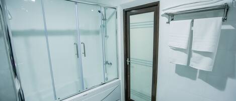 A bathroom with a glass-enclosed shower, a wooden door, and a towel rack with two towels.