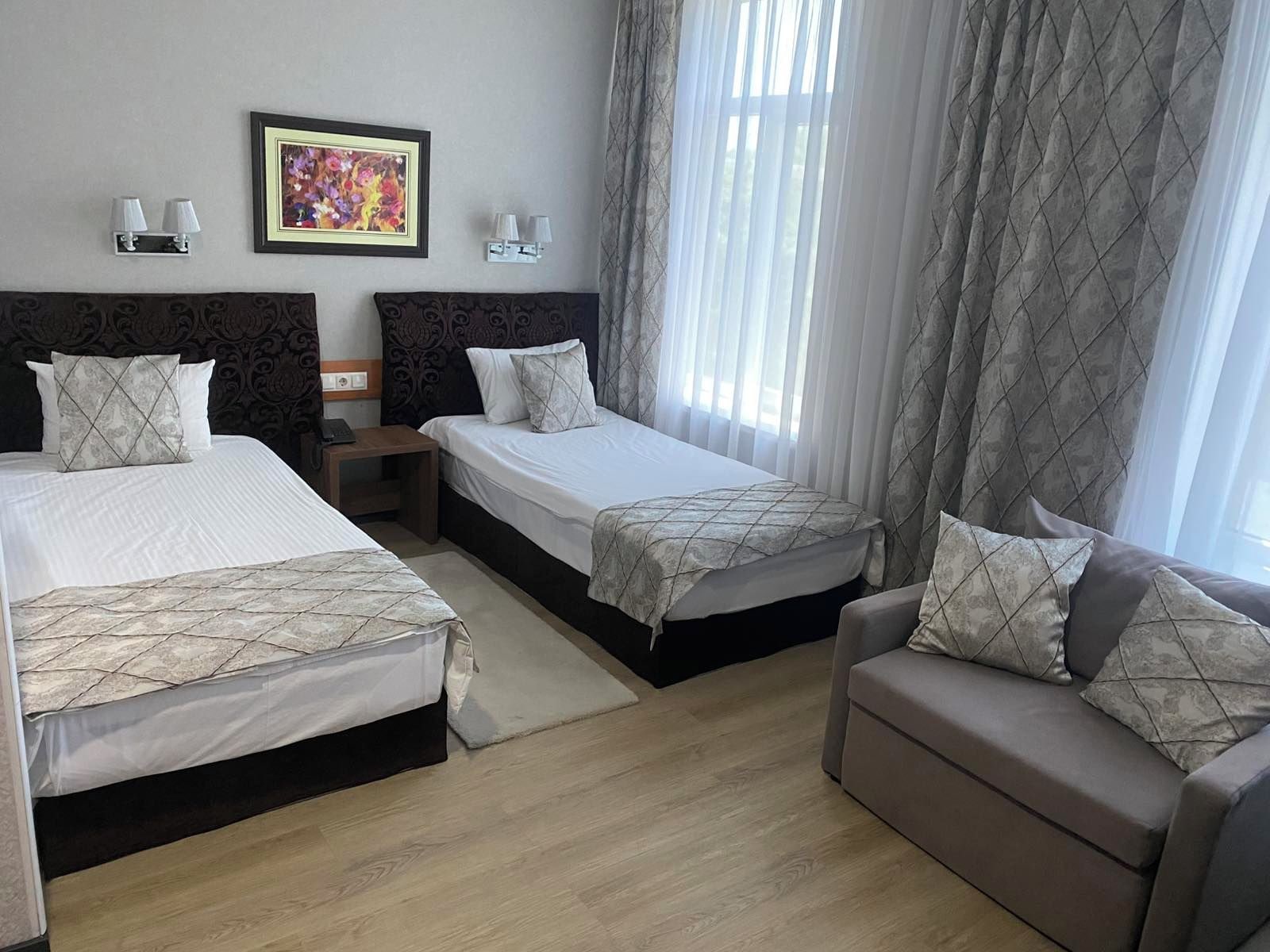A hotel room with two beds, a sofa, a nightstand, a framed picture, and a window with curtains.