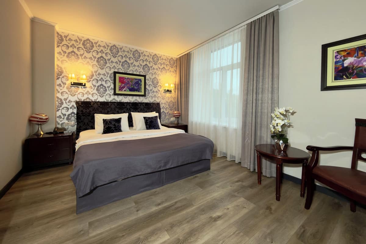 A hotel room with a large bed, a nightstand, a chair, and a small table.