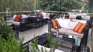 An outdoor seating area with wicker furniture and cushions, surrounded by greenery. - Aria Hotel Chisinau (Chisinau)