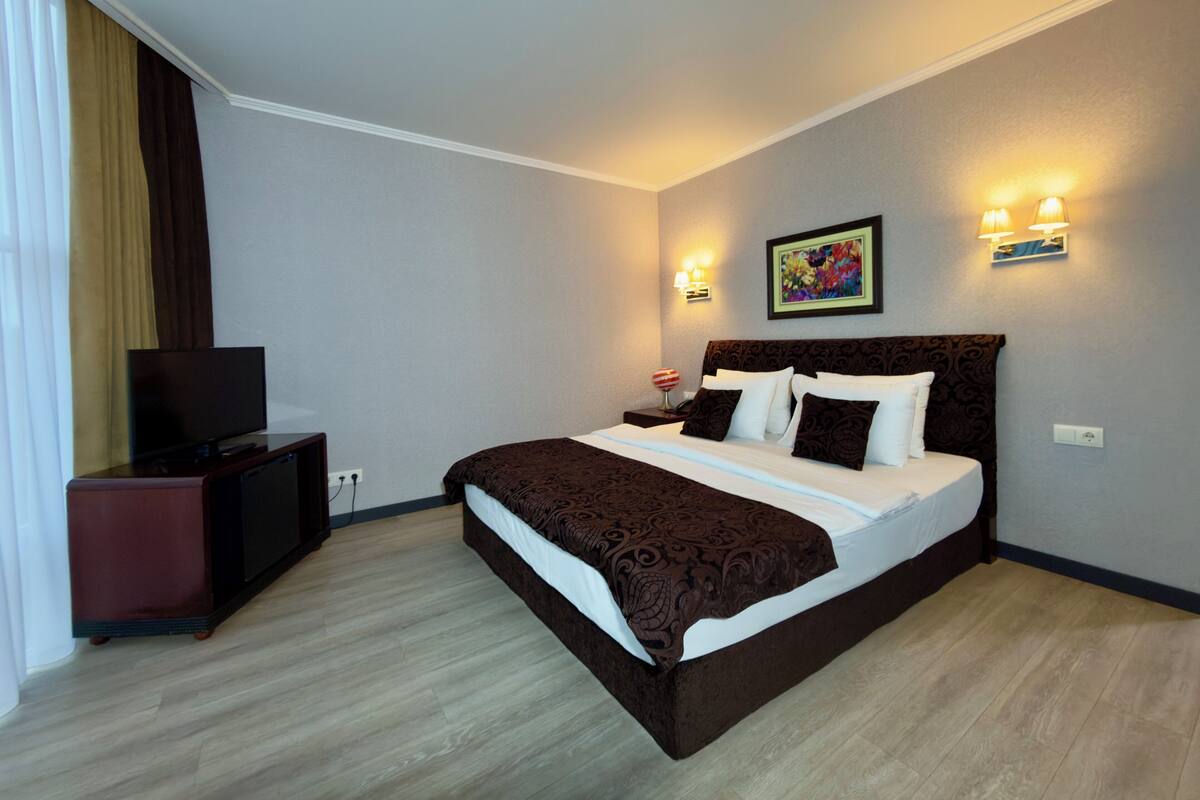 A hotel room with a large bed, a TV, a desk, and a painting on the wall.