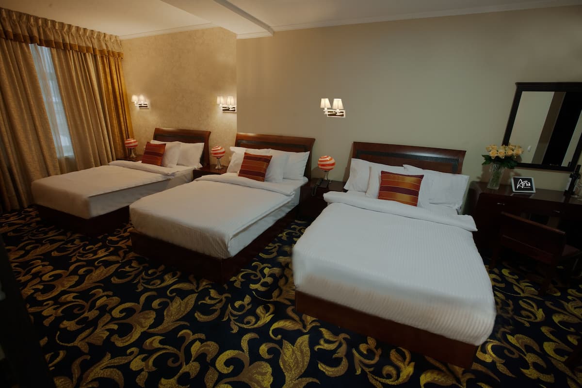A hotel room with three single beds, a large mirror, and a wooden nightstand with a vase of flowers.