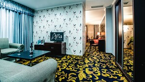 A hotel room with a patterned carpet, a sofa, a TV, and a minibar. - Aria Hotel Chisinau (Chisinau)