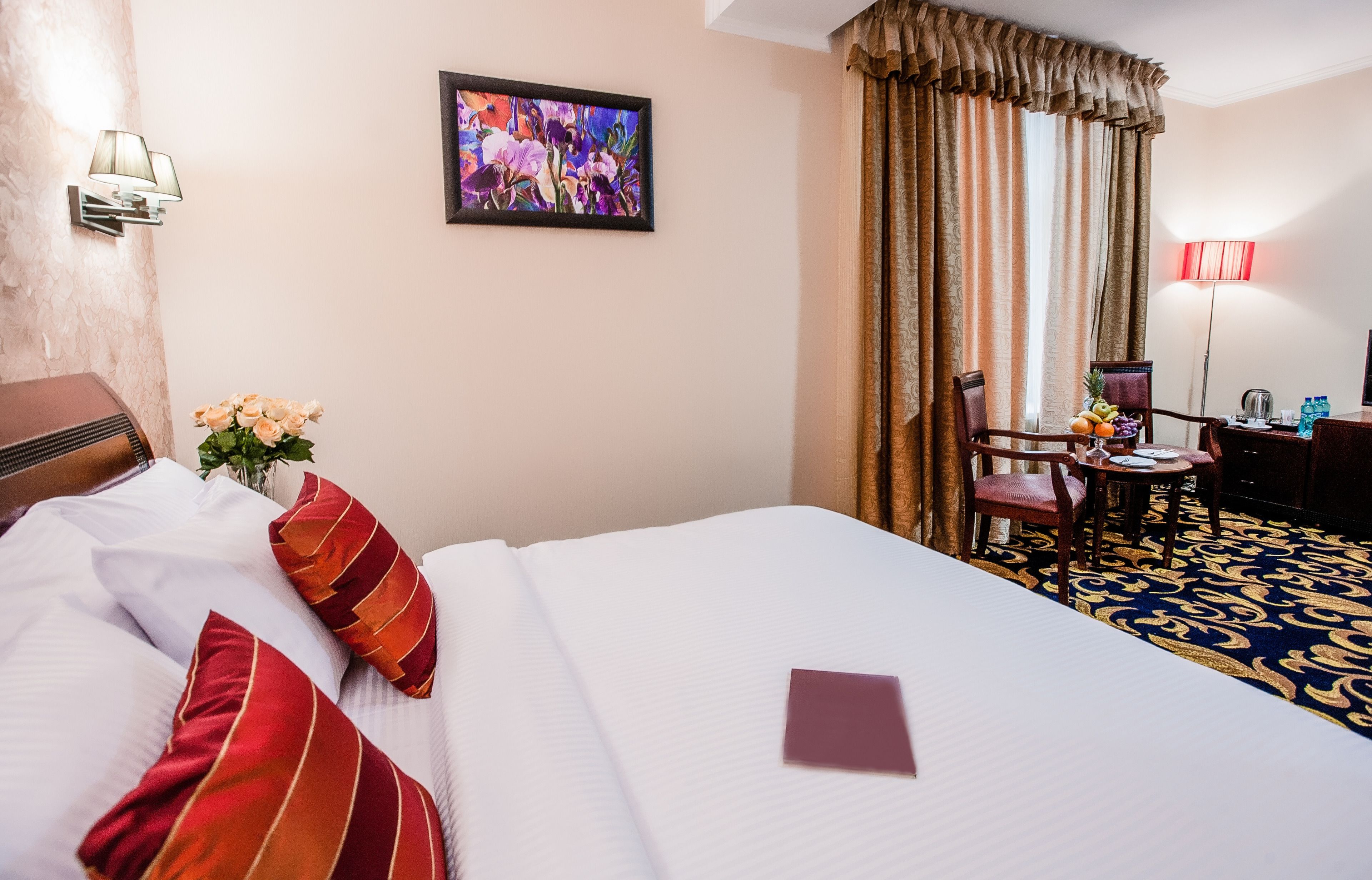 A hotel room with a bed, a desk, a chair, a lamp, a painting, and a window with curtains.