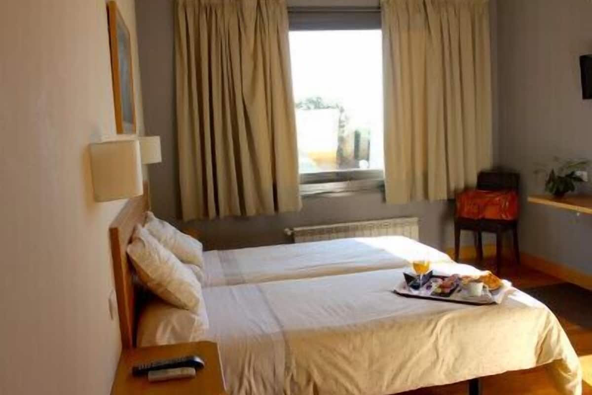 Habitación de hotel con dos camas, una mesita de noche con un control remoto, una bandeja con artículos de desayuno y una ventana con cortinas.