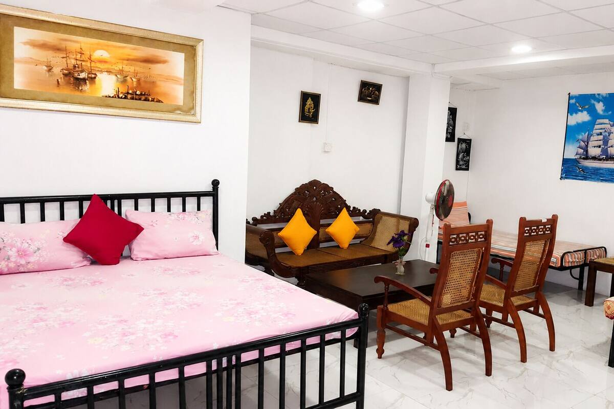 A hotel room with a bed, a wooden sofa, a dining table with chairs, and a wall with framed artwork.