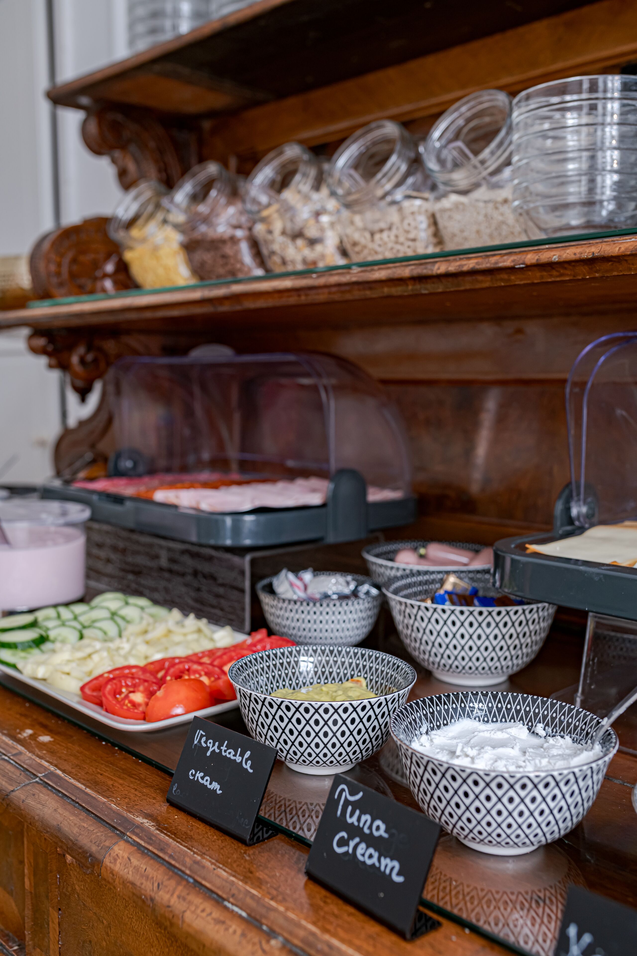 Un bufé con recipientes etiquetados de crema, verduras y otros alimentos.