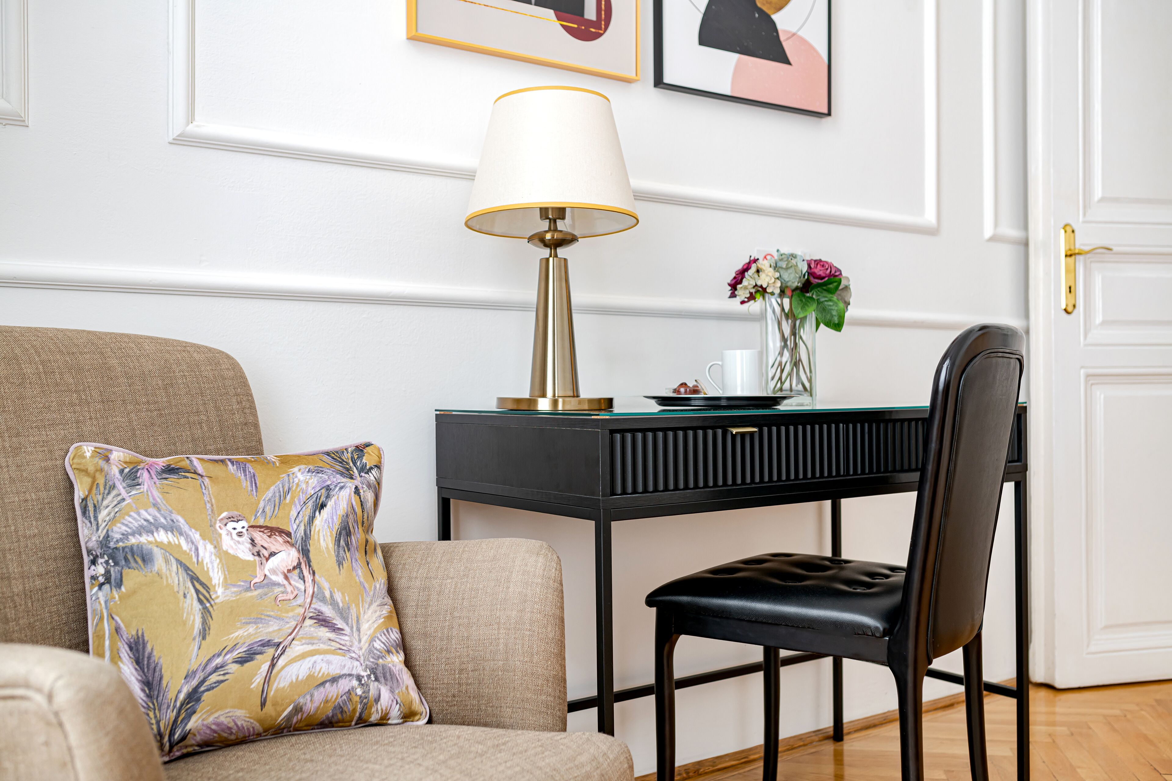 Un salon moderne avec un canapé, un fauteuil, un bureau avec une lampe et un vase rempli de fleurs.