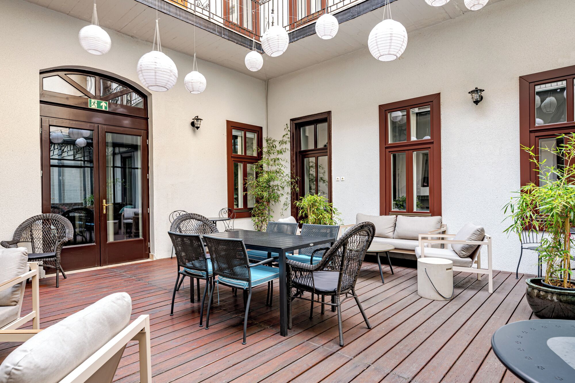 An outdoor patio with a wooden deck, a round table with chairs, a sofa, and potted plants.
