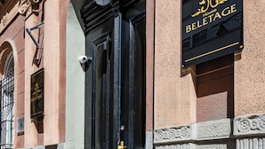 Une façade d’immeuble avec une porte noire, une enseigne indiquant « MAISON BELETAGE » et une petite fenêtre agrémentée d’un élément décoratif.