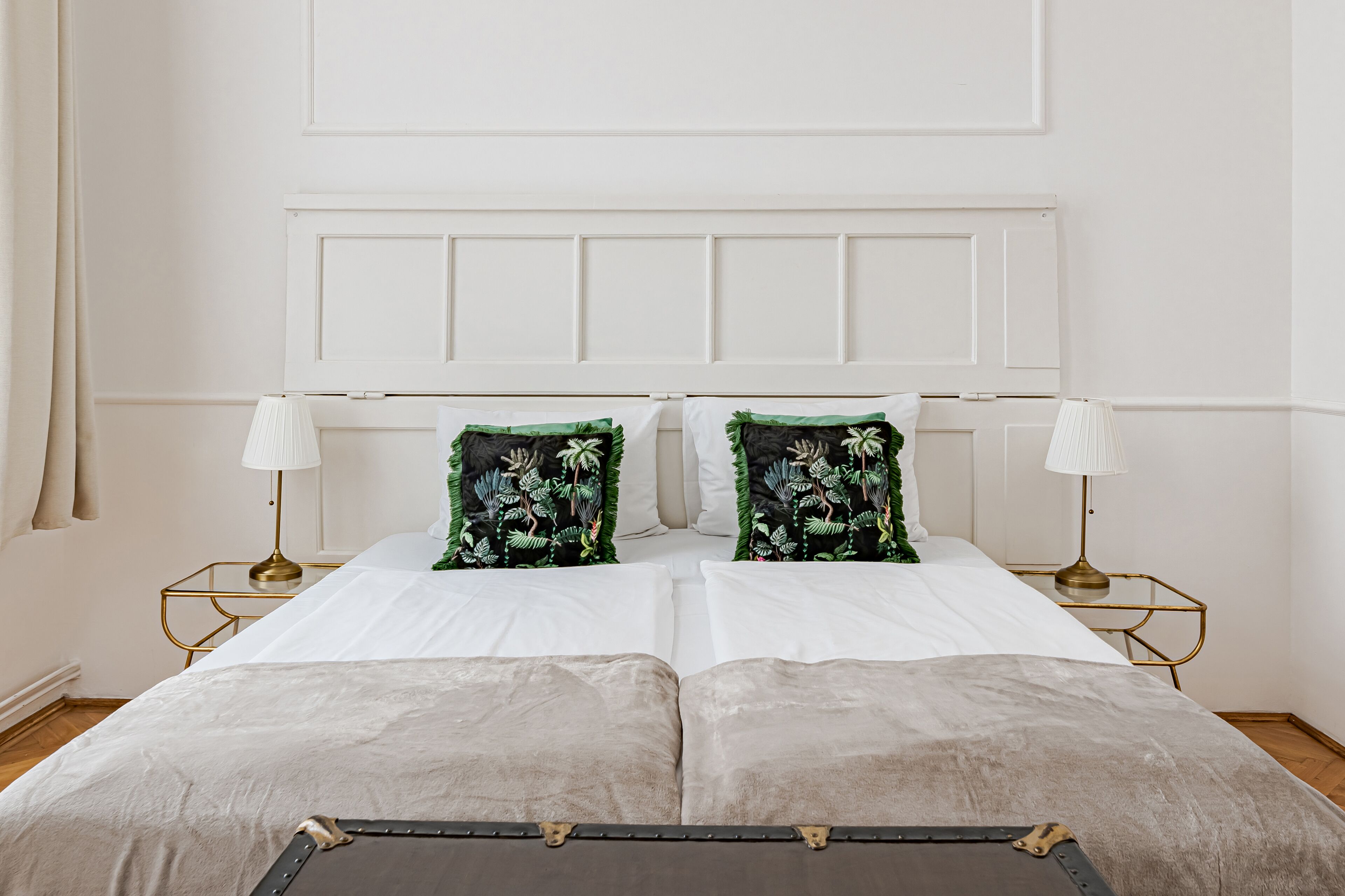 Una cama doble con ropa blanca, dos almohadas decorativas, lámparas de noche y un aparador.