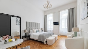 Une chambre d’hôtel moderne avec un grand lit, un bureau avec une chaise, une table ronde ornée d’un vase de fleurs et un téléviseur fixé au mur.