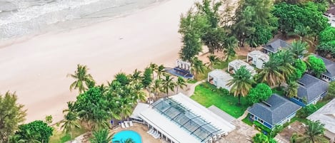 Vista aérea de un complejo turístico costero con piscina, playa y palmeras.