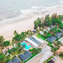 Vista aérea de um resort à beira-mar, com piscina, praia e palmeiras.