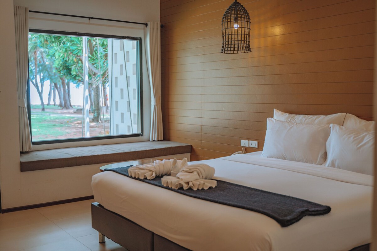 Une chambre d’hôtel avec un grand lit, une fenêtre donnant sur des arbres et un mur en bois.